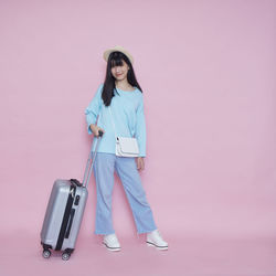Portrait of young woman standing against pink background
