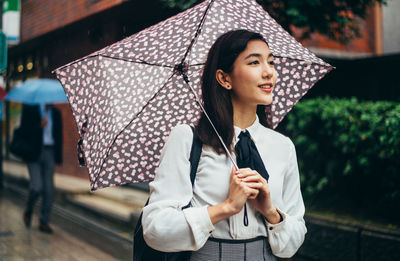 Beautiful young woman looking away while standing outdoors during rain