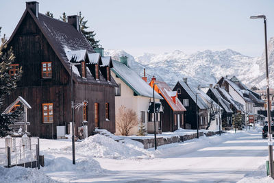 Houses on snow covered field by buildings against sky