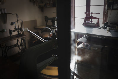 Back view of unrecognizable craftsman sitting working in dark workshop