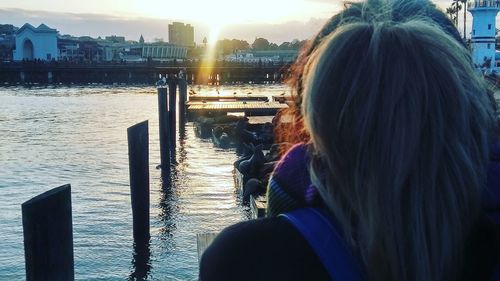 Rear view of woman sitting by cityscape against sky during sunset