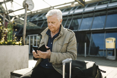 Businessman using smart phone while sitting on bench at railroad station