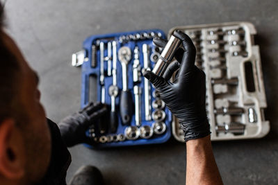 From above anonymous male technician in latex gloves selecting wrench bit from tool box during work in garage