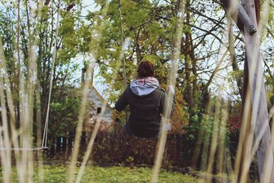 Rear view of woman sitting on swing in yard