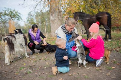 Happy family-mother with  children hugging and feeds pets dogs, cats and goats in countryside farm