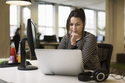 Businesswoman working on laptop at desk in creative office