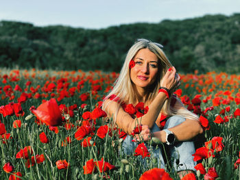Portrait of young woman with red poppy flowers on field