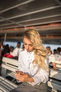 Beautiful young woman using mobile phone while sitting on bench