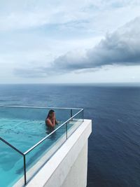 Woman in swimming pool by sea against sky