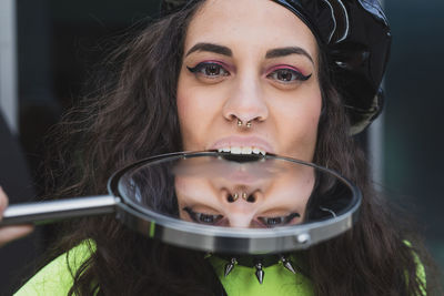 Close-up portrait of young woman biting mirror with reflection