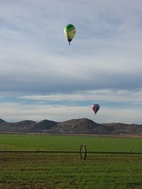 Hot air balloons flying over landscape against cloudy sky