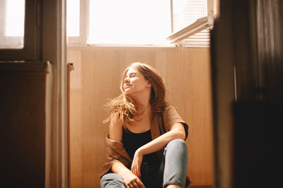 Young woman tossing hair while sitting on floor in balcony in summer