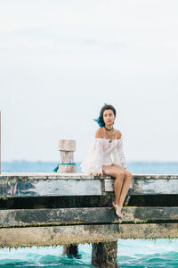 Full length of woman sitting on pier at beach against sky