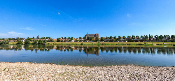 Scenic view of lake by buildings against blue sky