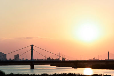 Suspension bridge over river against sky during sunset