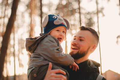 Happy father carrying playful son at park during sunny day in autumn