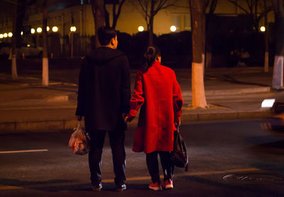 Rear view of couple walking on road at night