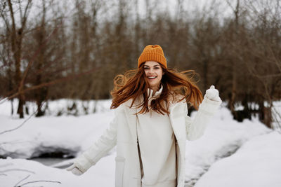 Portrait of smiling young woman standing on snow covered field during winter