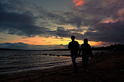 Silhouette friends standing on beach against sky during sunset