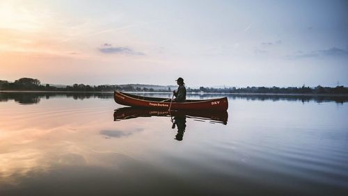 Man sitting on boat in lake against sky