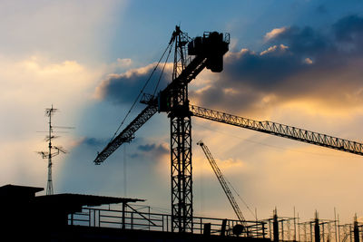 Low angle view of crane at construction site against sky during sunset