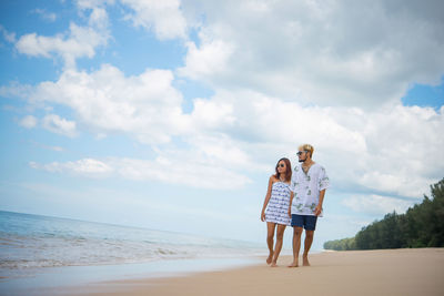 Man and woman walking at beach against sky