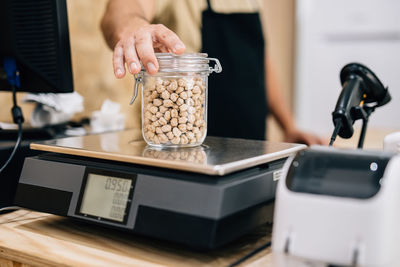 Anonymous shopkeeper checking weight of chickpeas on electronic scales