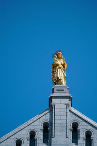Low angle view of virgin mary statue on building against clear blue sky