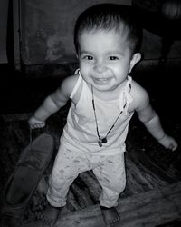 Portrait of cute smiling baby girl holding shoe while standing on floor