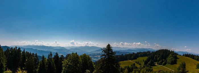 Panoramic view of trees and mountains against blue sky