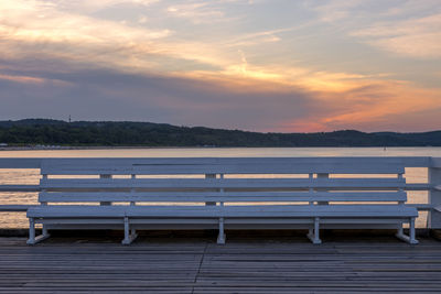 Empty bench by sea against sky during sunset