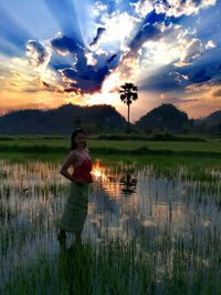 Woman standing on grass against sky during sunset