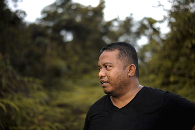 Portrait of man looking away against trees