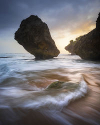 Rock formation in sea against sky during sunset