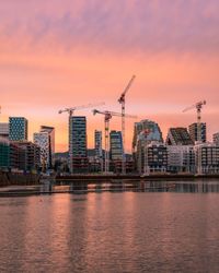 City by river against sky during sunset