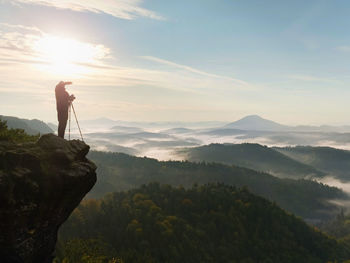Nature photographer in the action. man silhouette above a misty clouds, morning hilly landscape.