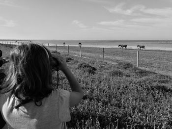 Rear view of girl looking at horses on meadow