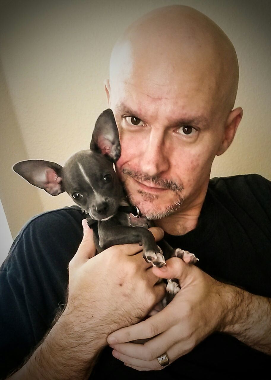 indoors, looking at camera, portrait, person, lifestyles, young men, leisure activity, animal themes, front view, home interior, casual clothing, holding, one animal, young adult, pets, togetherness, dog, headshot