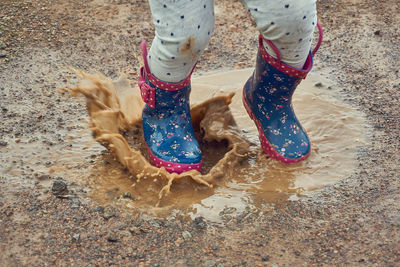 Low section of playful girl jumping in puddle on land