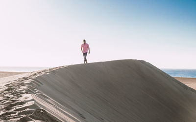 Rear view of man walking on beach against clear sky