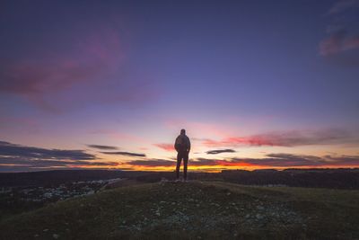 Rear view of man standing on mountain against dramatic sky during sunset