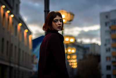 Portrait of young woman standing in illuminated city