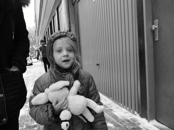 Portrait of girl holding stuffed toy while standing on footpath