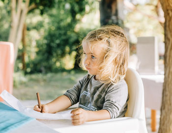 Girl looking away while drawing over paper on table