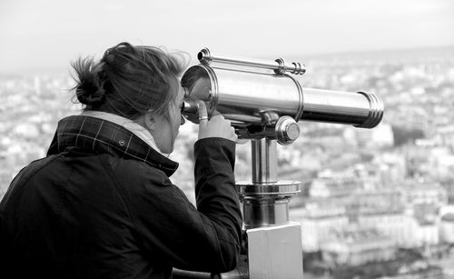 Woman looking through binoculars at city