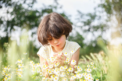 Sitting girl with dark short hair in yellow dress watching daisies in a sunny day