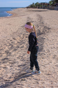 Beautiful little blond hair girl with long braid jumping on sea beach. smiling child walking on sand