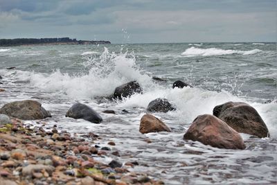 Waves splashing on rocks at shore against sky