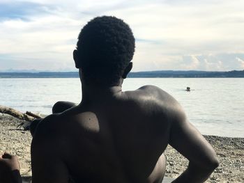 Rear view of shirtless man resting at beach
