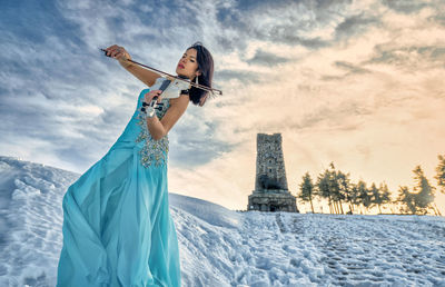 Woman playing on violin in snow against sky